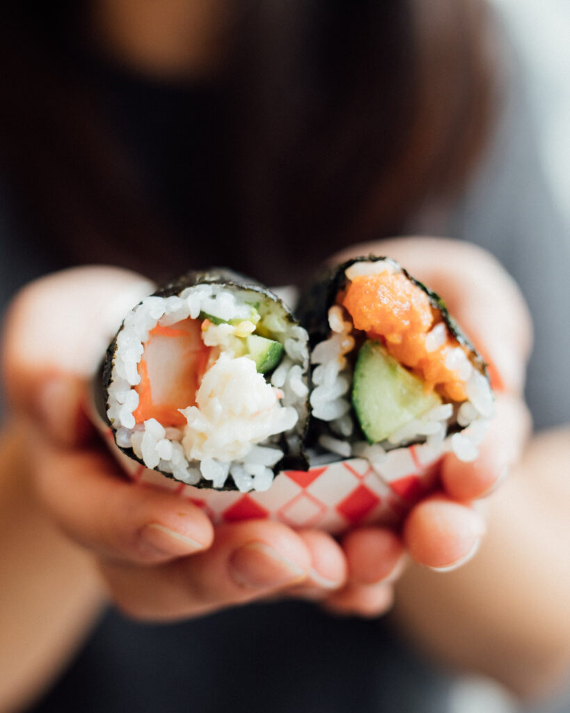 Hands holding two fresh salmon and cucumber sushi rolls