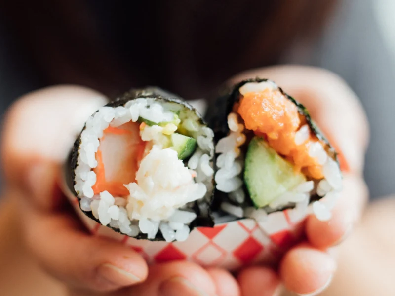 Hands holding two fresh salmon and cucumber sushi rolls