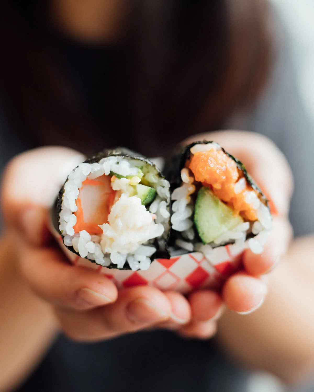 Hands holding two freshly made salmon and cucumber sushi rolls, showing the rice, nori and filling
