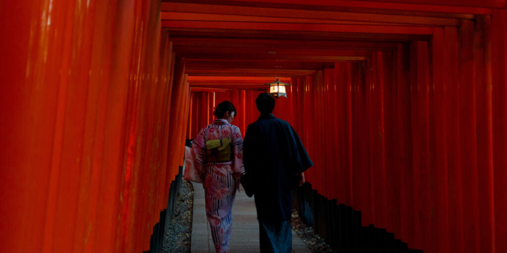 Two people walking through red torii gates
