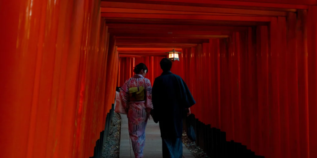 Two people walking through red torii gates